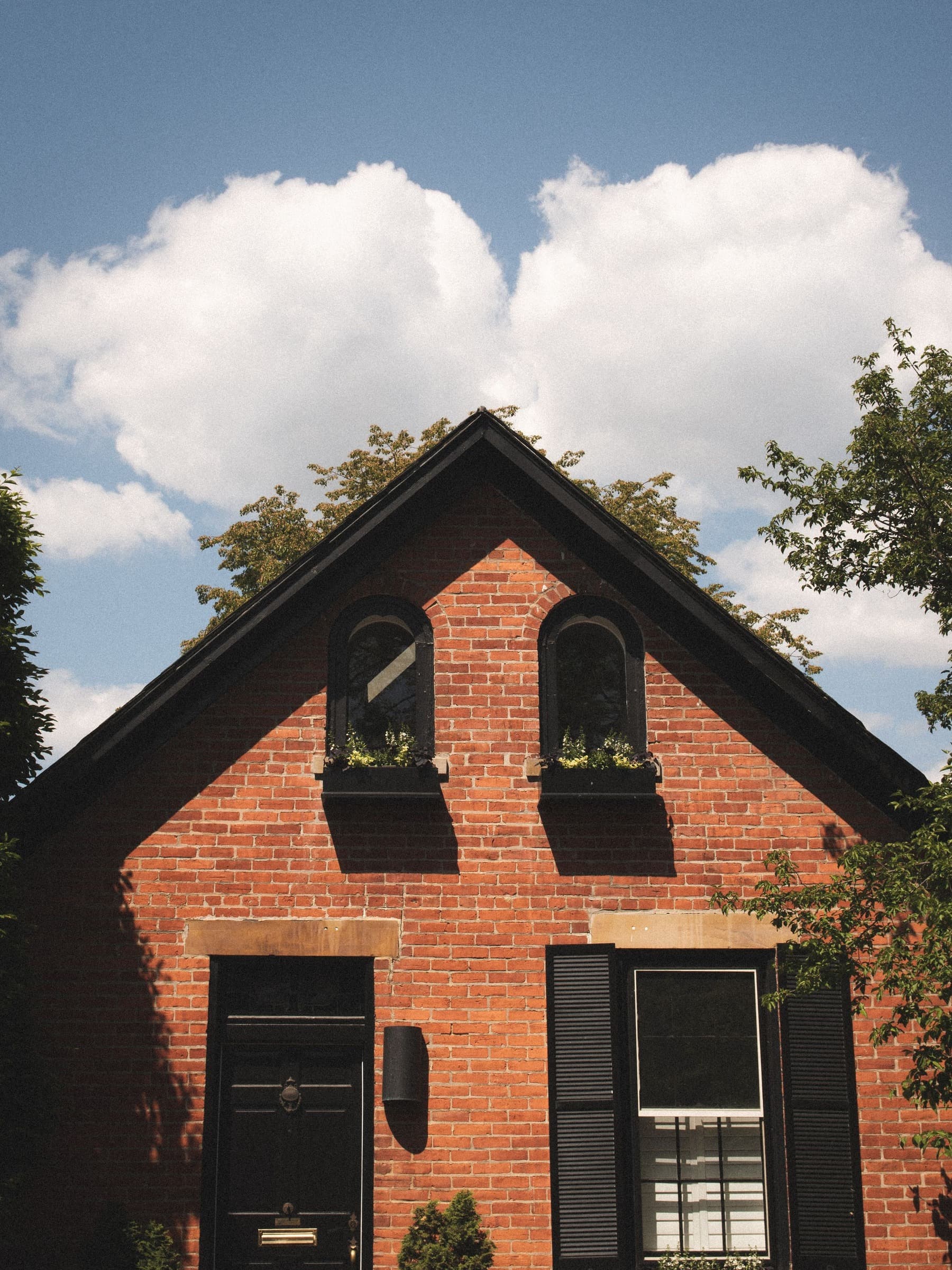 Red brick home with a steep gable, black shutters and a blue sky