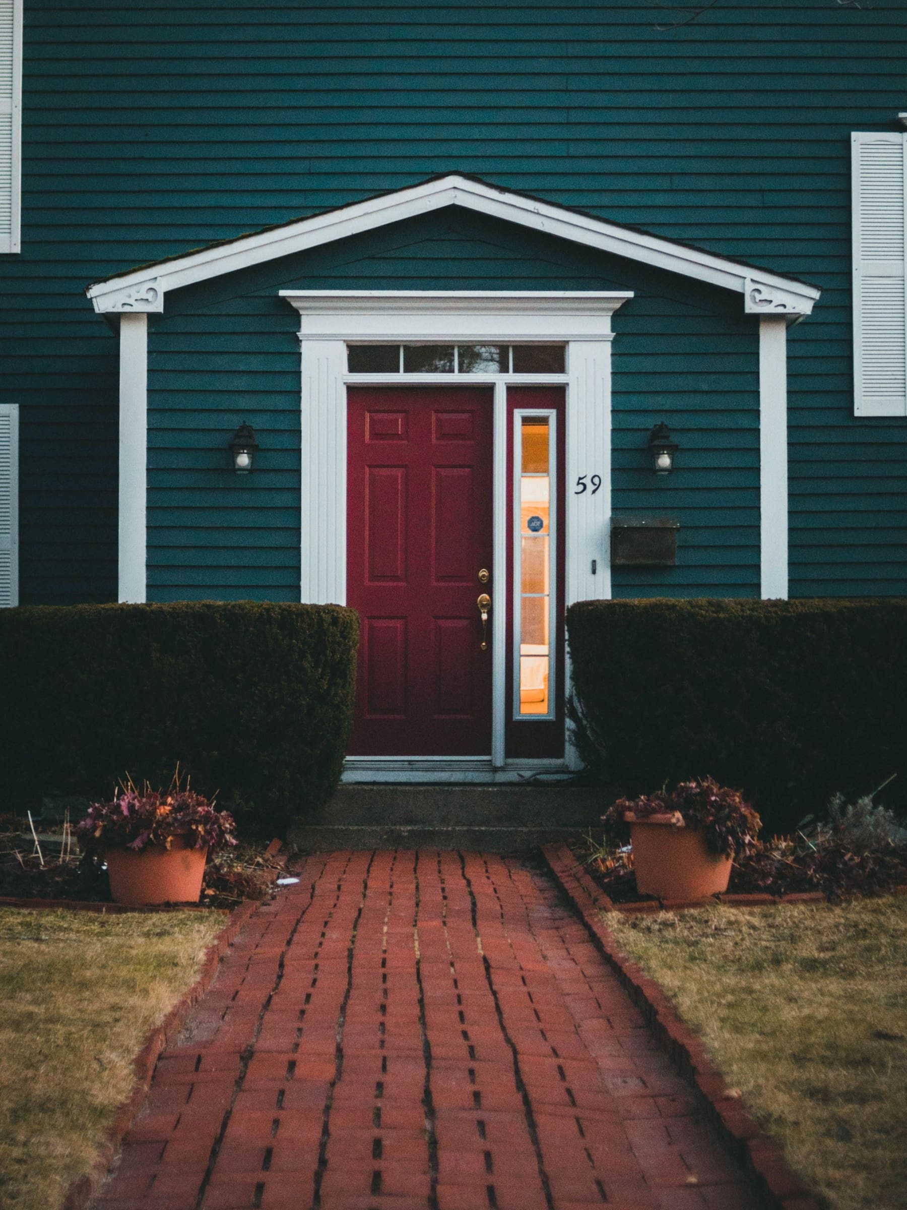 Clean red brick walkway leading to a teal clapboard house with a red front door