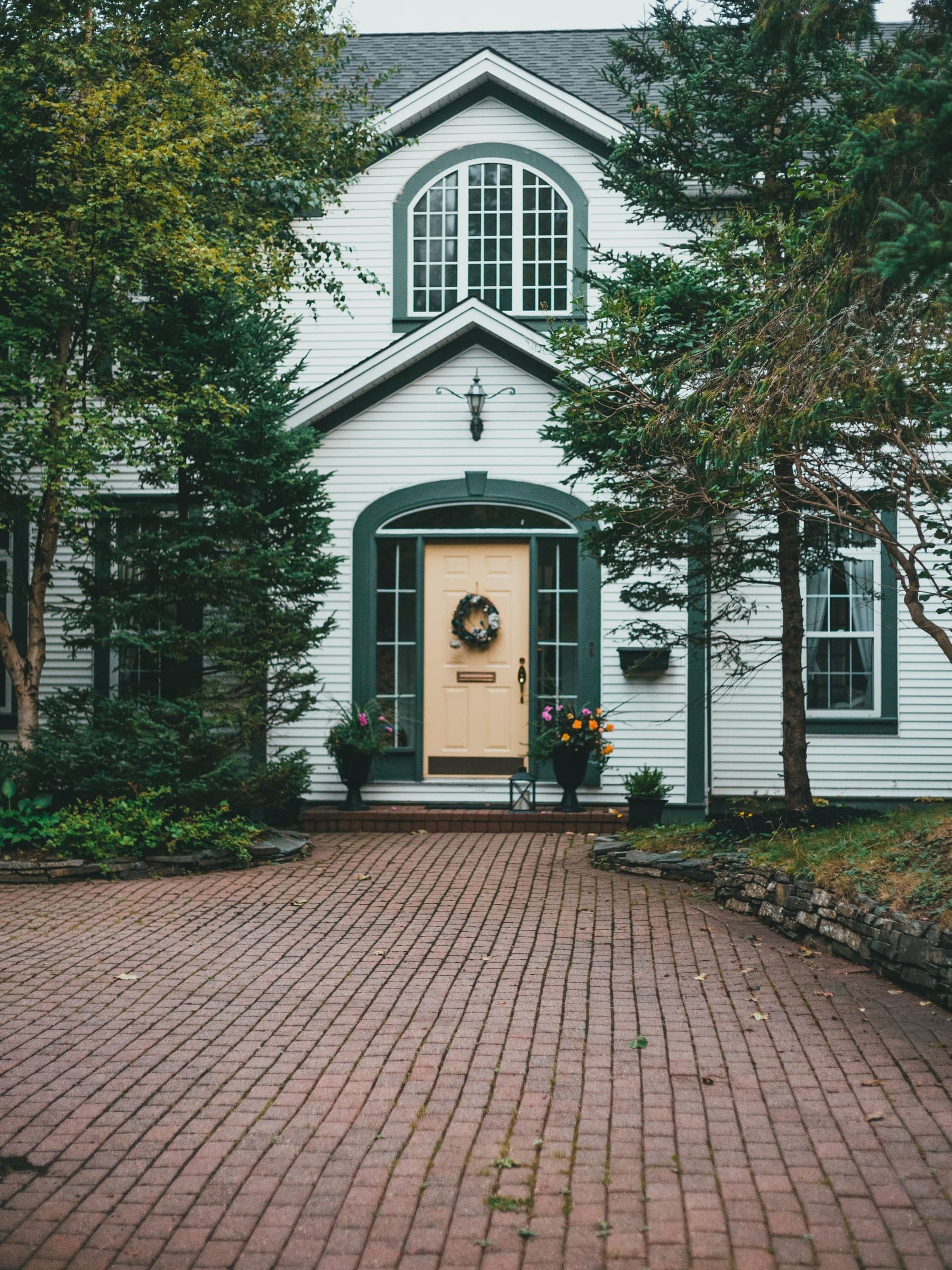 White colonial-style home with green trim and a brick-paver driveway