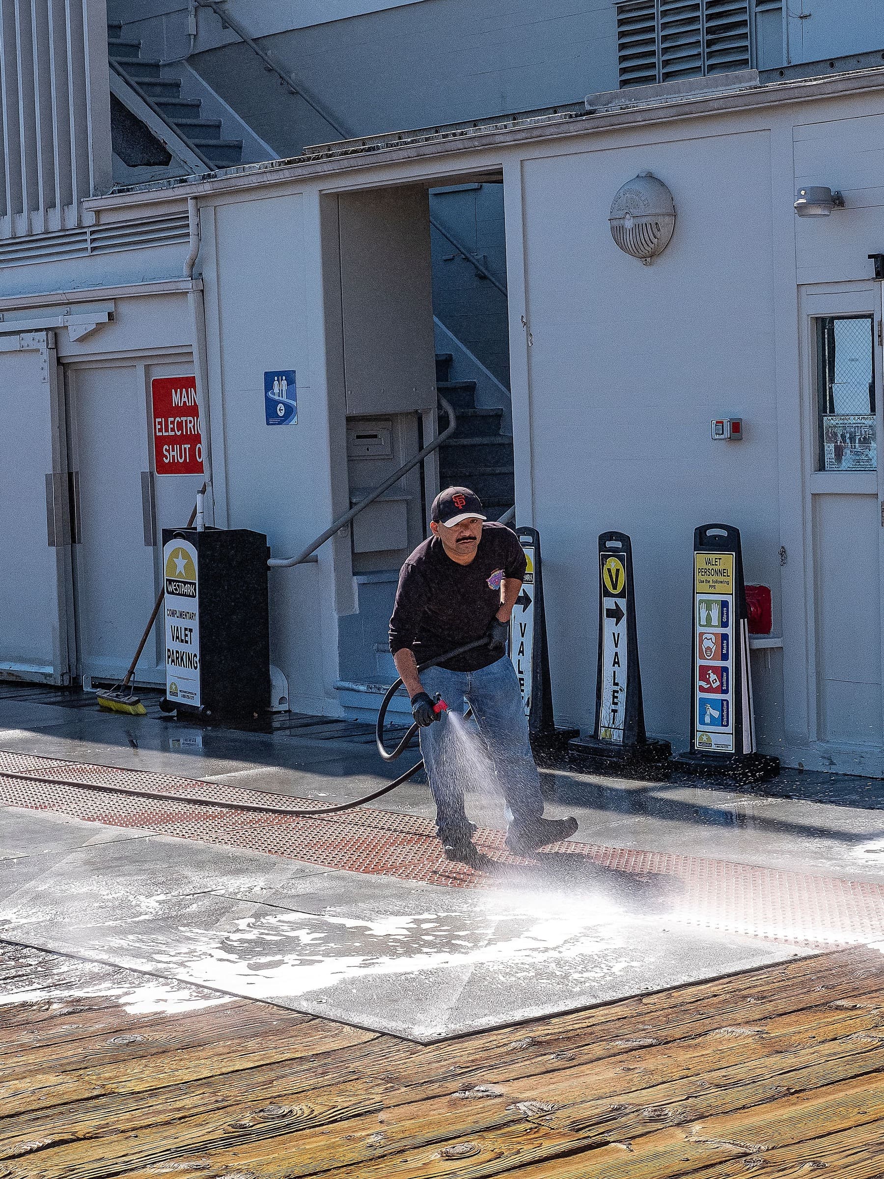 Worker pressure washing soapy pavement outside a white commercial building