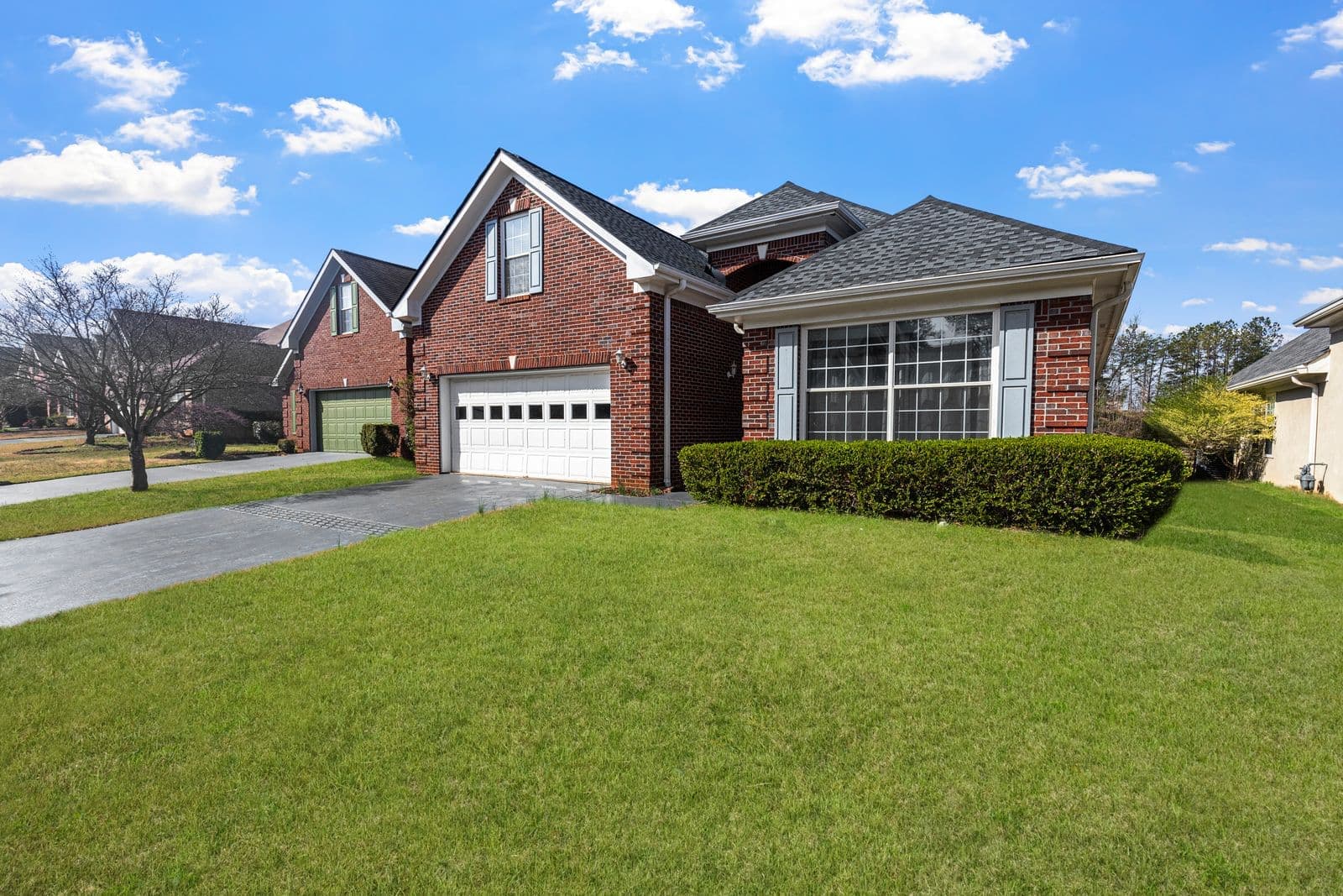 Red brick suburban home with a white garage door and a trimmed lawn