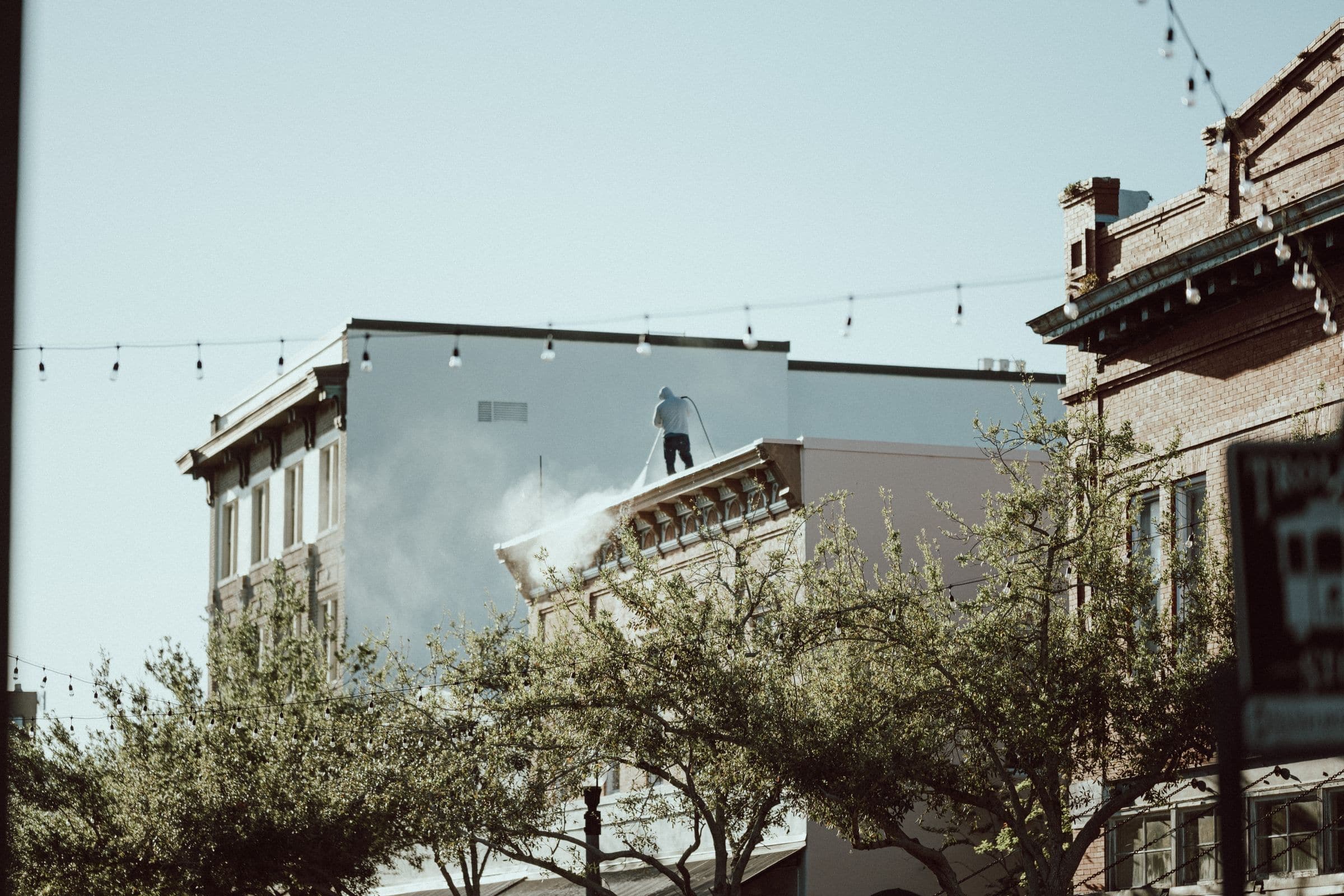 Worker on a rooftop pressure washing the facade of a downtown commercial building