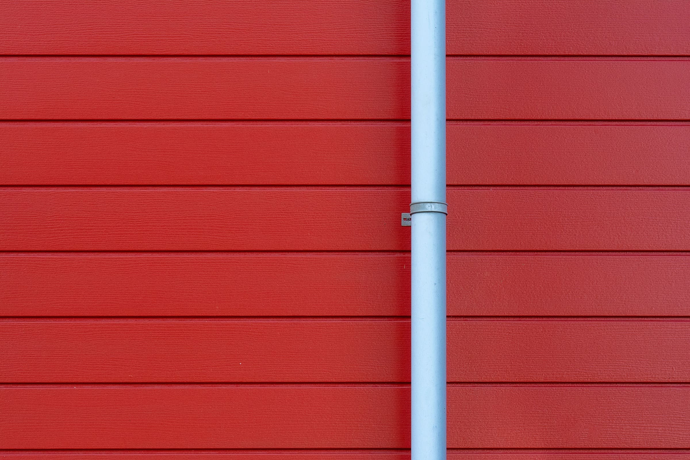 White downspout on clean red siding, part of the gutter line that gutter cleaning keeps flowing